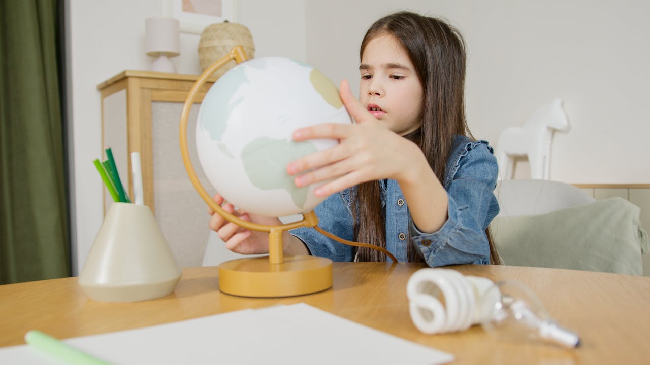 Mastering the First Impression: Your intriguing post title goes here A young girl in a denim shirt examines a globe at a desk indoors, symbolizing learning and exploration.